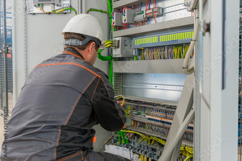 Electrician builder at work inspecting cabling connection of high voltage power electric line in industrial distribution fuseboard. Engineer works with electric cable wires of fuse switch box