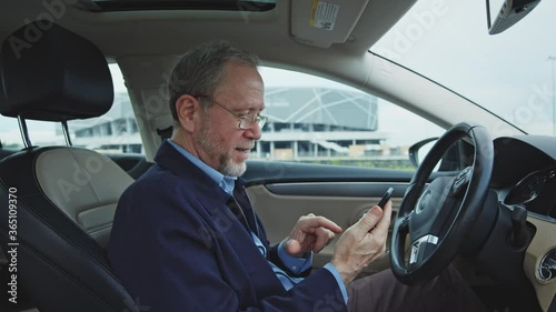 Bearded nice-looking senior businessman stops on the road, sitting in expensive modern car, reading messages from grandchildren and smiling with much joy. Successful entrepreneur. Retirement