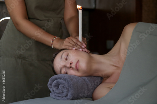 Woman receiving ear candle treatment at spa. Ear coning or thermal-auricular therapy. photo