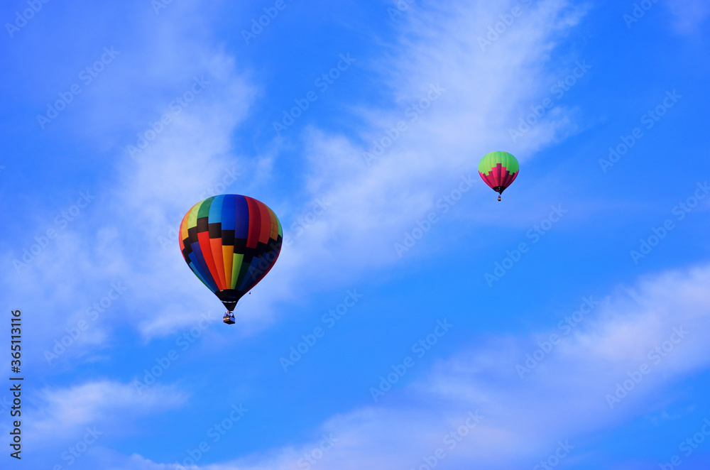 Naklejka premium Two multicolored balloons fly high in the sky against a backdrop of white clouds and blue sky