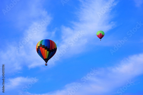 Two multicolored balloons fly high in the sky against a backdrop of white clouds and blue sky