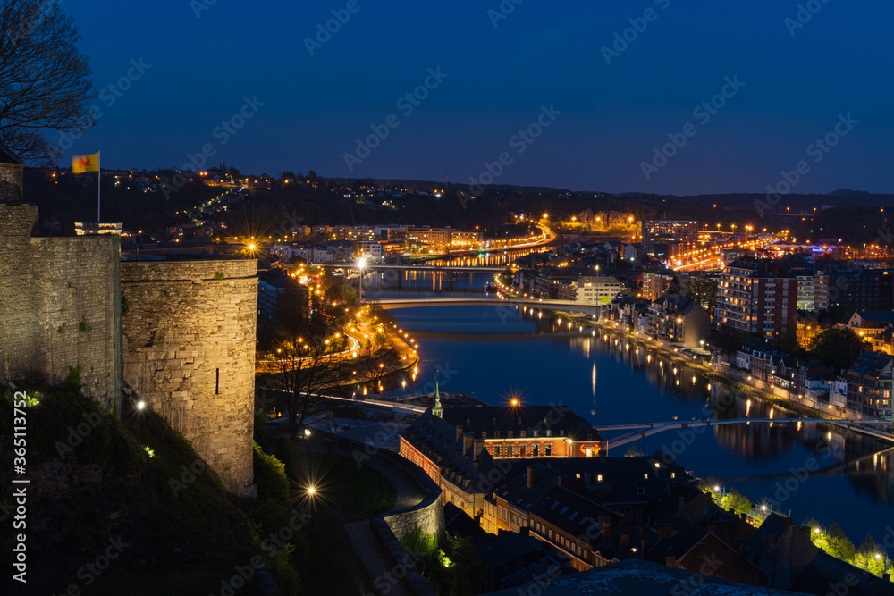 The citadel of Namur and the city lights with car lights on slow speed and the reflection on the Meuse river.