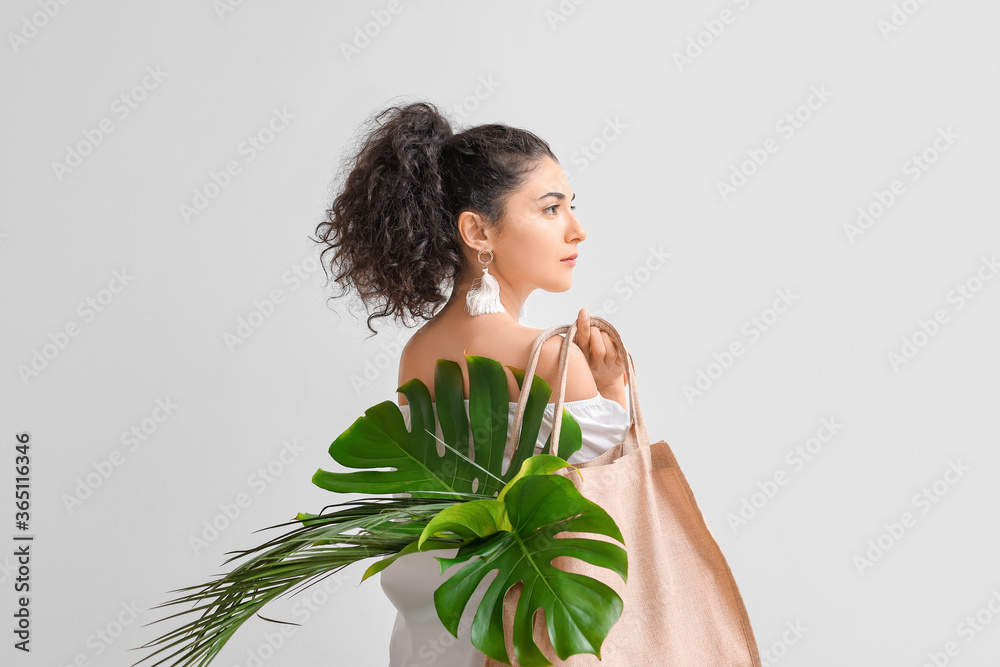 Beautiful young woman with tropical leaves in eco bag on light background Beautiful young woman with tropical leaves in eco bag on light background