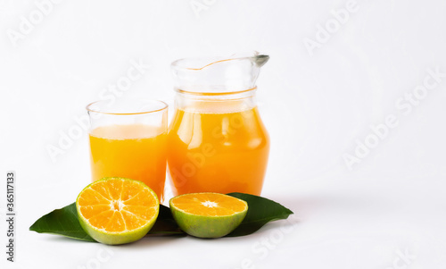 Fototapeta Naklejka Na Ścianę i Meble -  Jug, glass of orange juice and orange fruits with green leaves  on white background