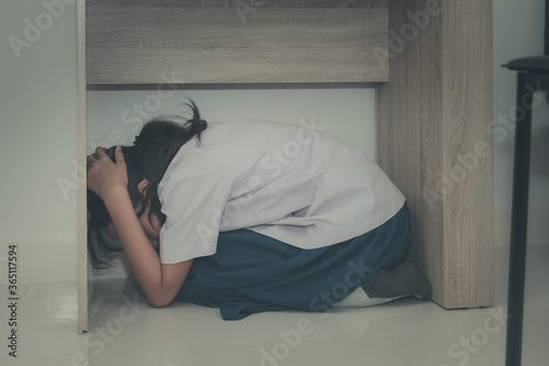 Asian young girl in a school uniform hides under the desk when an earthquake occurs with concept
