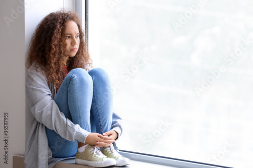 Sad African-American woman sitting on window sill. Stop racism