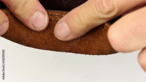 human hand testing piece of brown natural smooth shiny glossy leather with brown seams, the outer part and inside, part of backpack, check quality control of product, close-up macro view