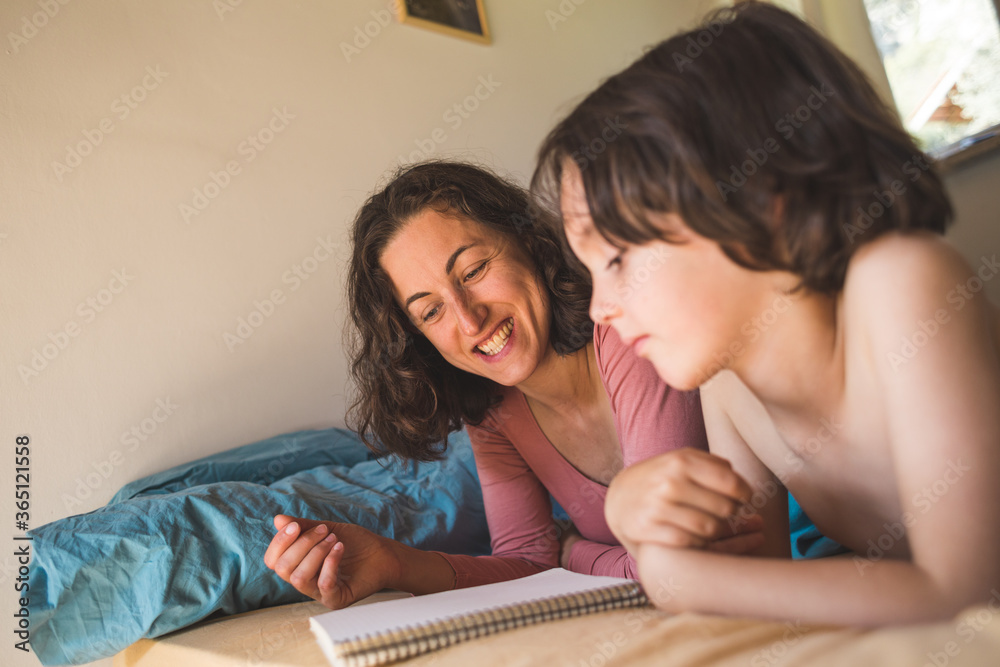 A boy with his mother lies in bed and reads a book. A boy with his mother lies in bed and reads a book.