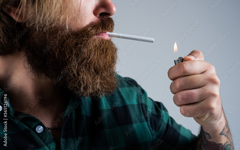 Fototapeta premium lightng the cigarette. bearded man. smoking cigarette habit. brutal hipster with moustache. fashion model in casual clothes. male beauty standard. looking so trendy. Confident and handsome brutal man