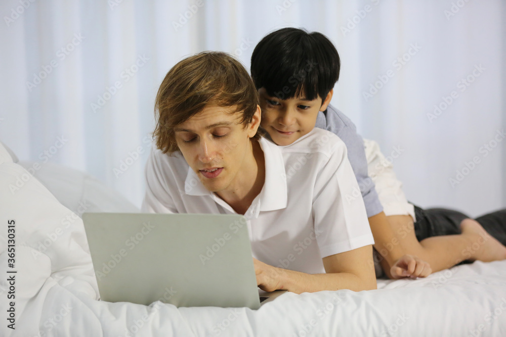 Closed up view of caring father teaching his son on laptop. Family is sitting in comfortable bedroom in house Closed up view of caring father teaching his son on laptop. Family is sitting in comfortable bedroom in house