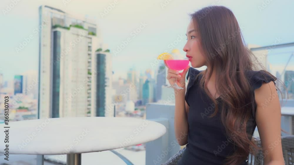 Against the backdrop of a modern urban skyline, a gorgeous woman sips from an exotic cocktail.