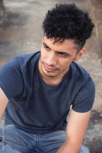 Portrait of young hispanic man sitting looking aside - thoughtful young man on rooftop in cloudy afternoon