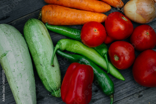 A variety of fresh vegetables, tomatoes, onions, zucchini, carrots, red and green peppers, on a rustic wooden table.