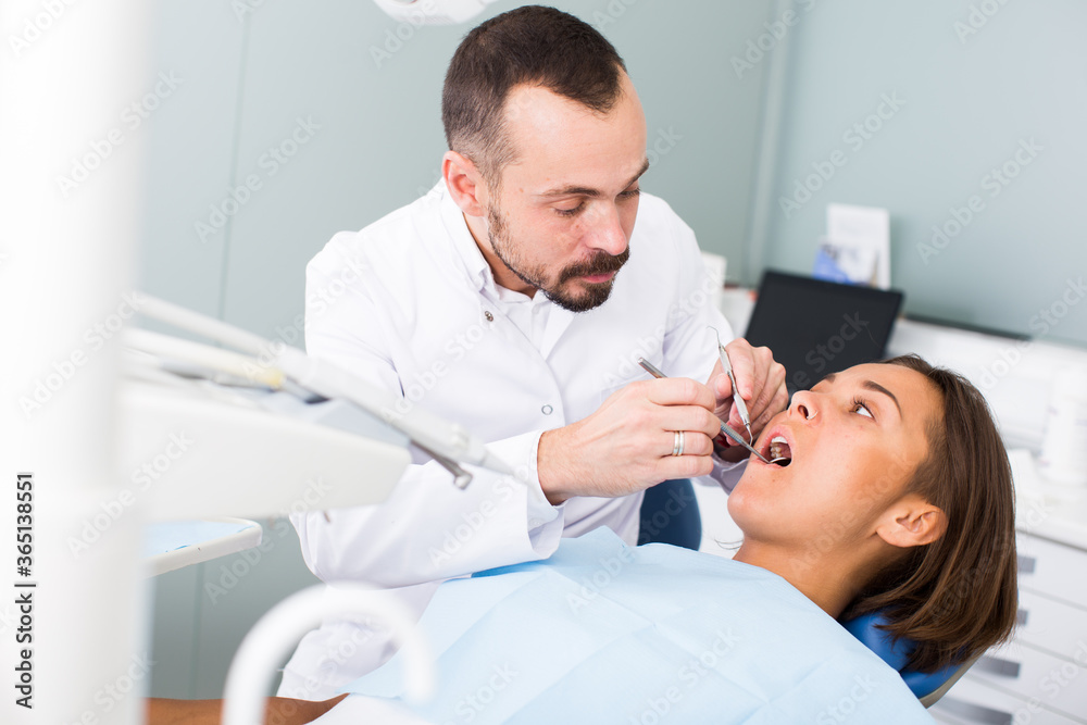 Fototapeta premium mężczyzna Dentysta leczy pacjenta siedzącego na fotelu dentystycznym w klinice