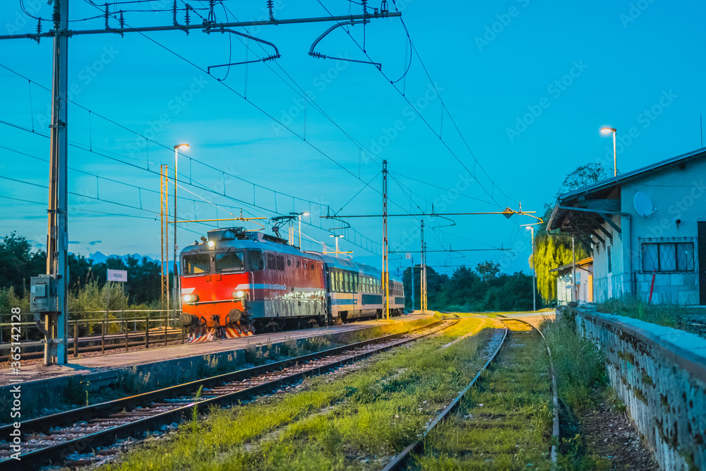 Passenger train hauling classical passenger coaches at night on a station of Preserje in Slovenia. Evening setting of an older type of train.