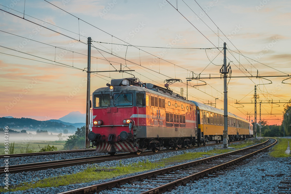 Night passenger train from Prague to Rijeka on its way over the Ljubljana marshes in early romantic morning with sunrise. Fast overnight express to Dalmatia.