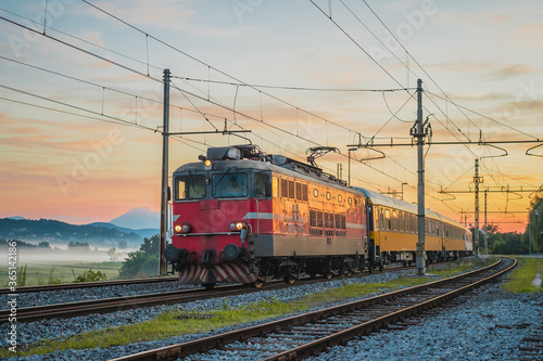 Night passenger train from Prague to Rijeka on its way over the Ljubljana marshes in early romantic morning with sunrise. Fast overnight express to Dalmatia. © Anze