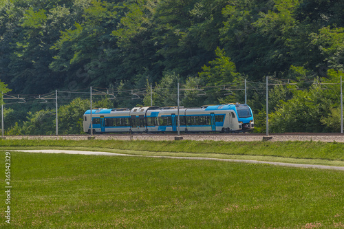Modern and new passenger swiss made Train in white and blue color is traveling on a dual track railway line in the rural setting on a sunny hot day. photo