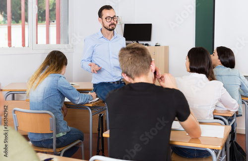 Young man teacher is giving interesting lecture for students in the classroom