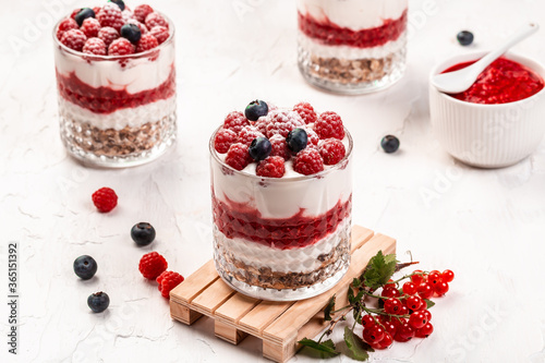 jars with tasty parfaits made of granola, berries and yogurt on white table. Healthy raspberry fruit dessert, place for text, banner