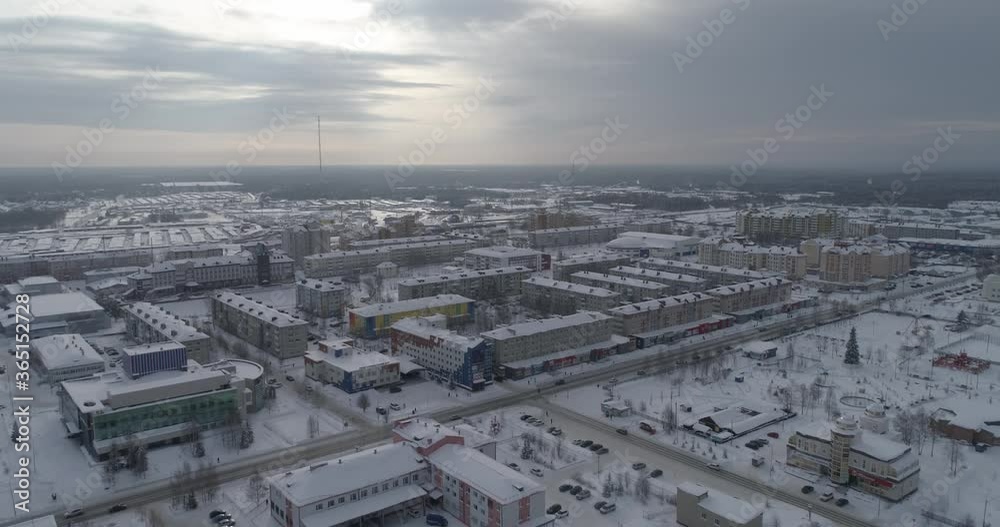 Aerial view of winter city. In the shot are residential buildings and office buildings. There is snow on the roads, cars drive on the roads. Beyond the city endless forests. Yugorsk city, Khanty Mansi