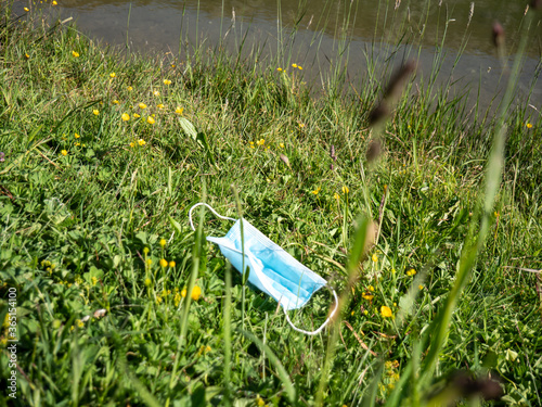 Low angle shot of a surgical face mask that has been discarded onto a grassy bank in nature.