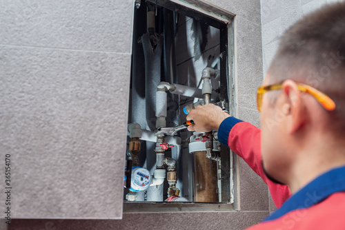 The man is installing the water supply system in the house and checking pipes by the wrench