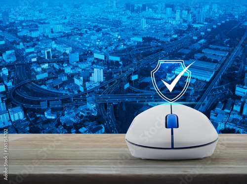 Security shield with check mark flat icon with wireless computer mouse on wooden table over modern office city tower  street  expressway  and skyscraper  Technology internet cyber security and anti vi