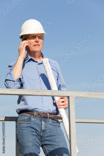 Engineer or architect with hard hat and blueprint in his hand on a construction site