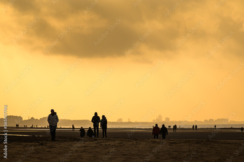 Silhouettes of people on the beach at sunset under cloudy sky.