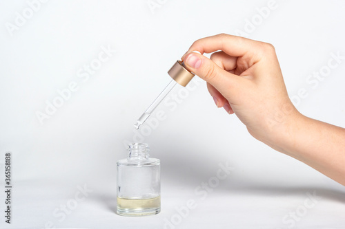 Pipette dropper with drop of natural oil above glass bottle on white background. Natural organic skin care beauty products.
