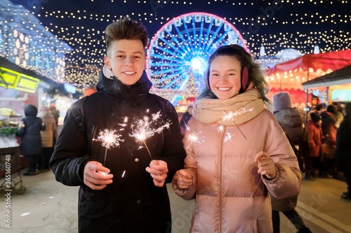 Happy teenage couple with sparklers celebrating and having fun at Christmas market