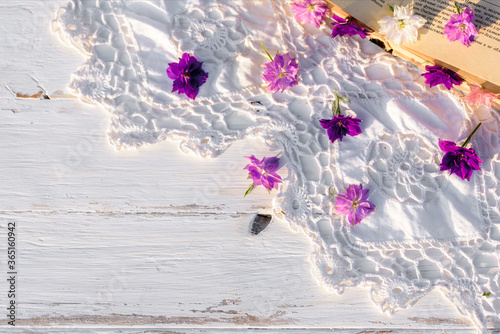 Violet flowers on a book. openwork knitted tablecloth on a wooden old table. evening in the village. sunset outdoors, batanica, beautiful flowers gelichrysum in the glass photo