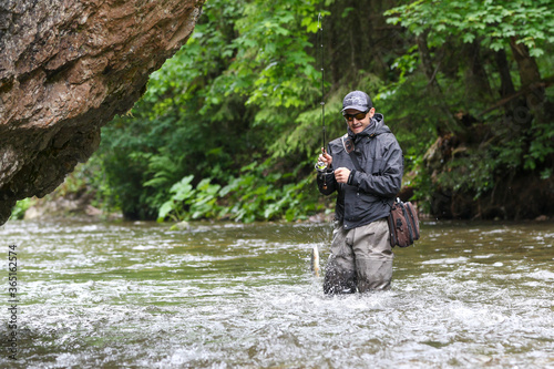 Fisherman in action fight against a trout. Fishing scene. Catch of fish.