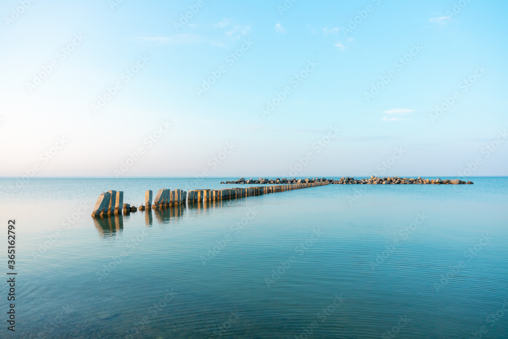 Calm morning sea surface with old stone pier and rocks. Morning seascape.
