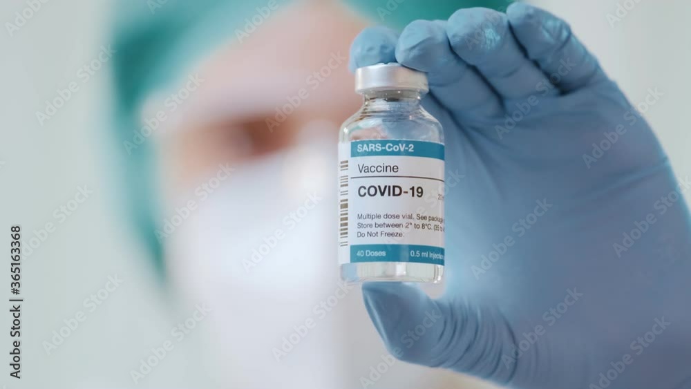 Young woman doctor holds in her hand vaccine bottle for COVID-19 new coronavirus, dressed in hazmat suit, protective mask KN95, medical goggles and rubber gloves in research laboratory, or hospital Young woman doctor holds in her hand vaccine bottle for COVID-19 new coronavirus, dressed in hazmat suit, protective mask KN95, medical goggles and rubber gloves in research laboratory, or hospital