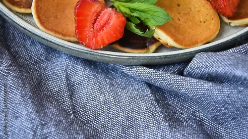 Mini pancakes rotating in bowl. Trendy food - tiny panckaes or baby cereal pancakes served strawberry and mint leaf. Selected focus. Close up photo