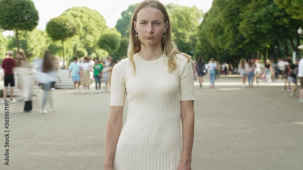 Time lapse of attractive woman standing in city center in busy street looking at camera wearing while crowds of people are walking by.