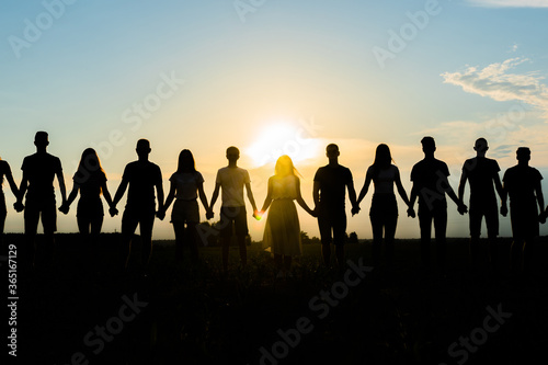 Cohesion concept. Black silhouettes of friends holding hands stands at sunset.