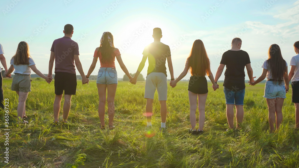 Fototapeta premium Cohesion concept. A group of friends are holding hands at sunset.