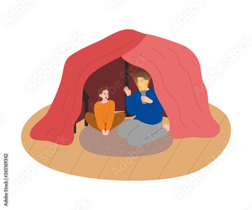 Father and son sitting in handmade cloth cave with flashlight and talking