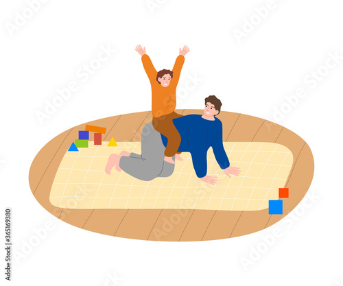 Happy son riding on fathers back on floor and having fun