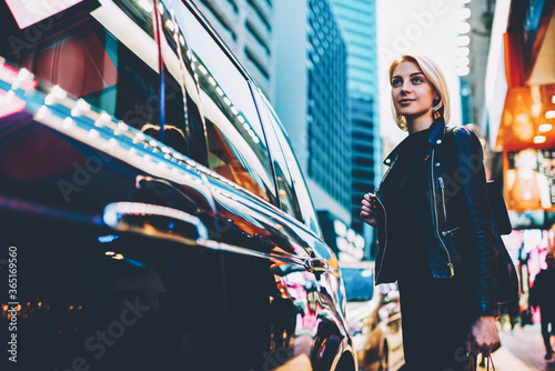 Charming young woman strolling outdoors on shopping streets and enjoying showplaces during vacantion.Good looking female tourist waiting transfer to destination standing in urban setting photo