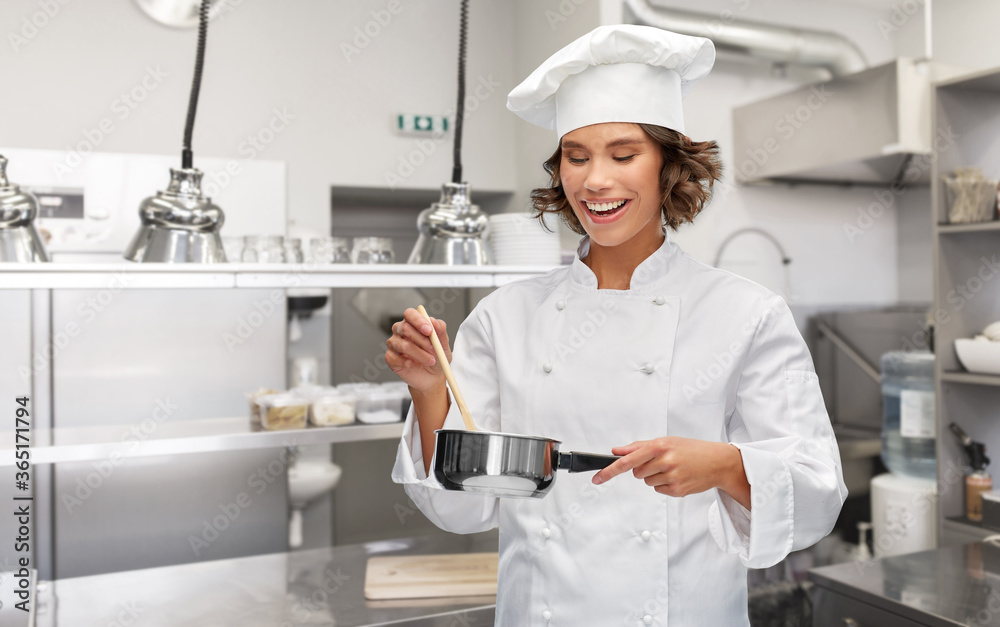 cooking, culinary and people concept - happy smiling female chef in toque with saucepan over restaurant kitchen background