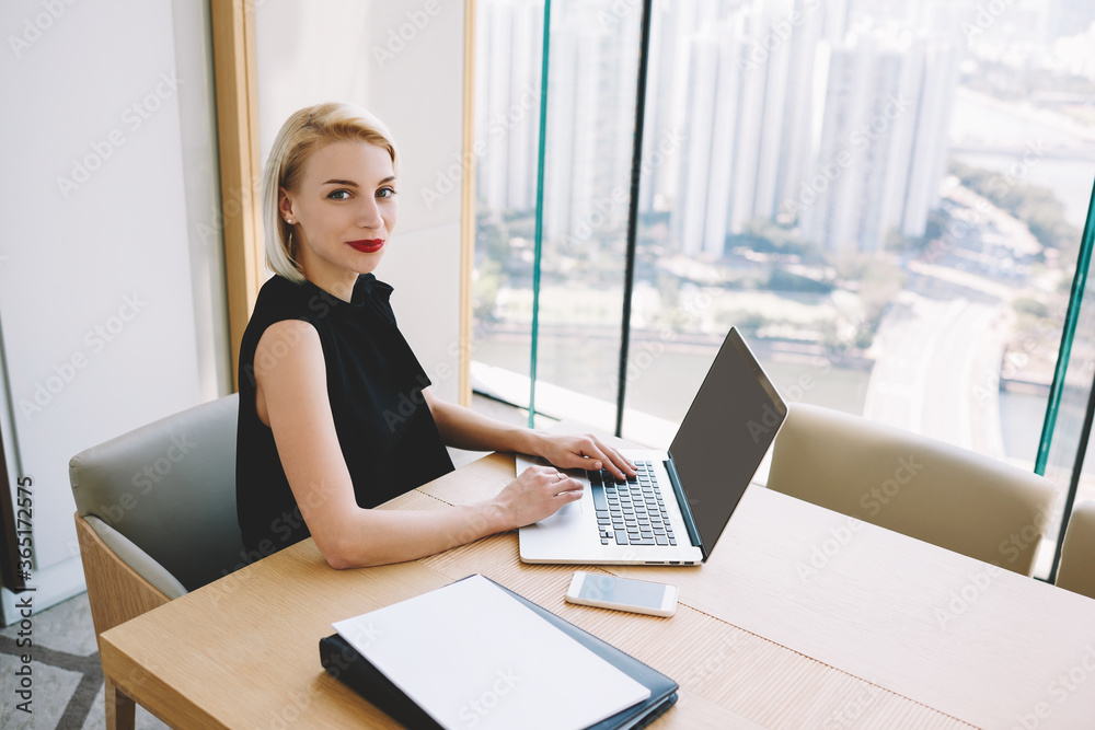Fototapeta premium Smiling blonde female executive manager searching information for project planning on laptop computer, portrait of smiling prosperous business woman making payment online via application for banking
