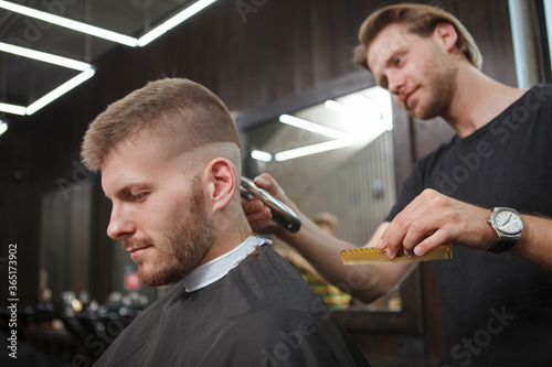 Handsome cheerful man getting a haircut done by professional barber