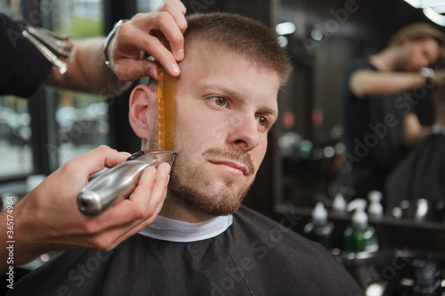 Male customer at the barbershop, getting beard trimmed by professional barber