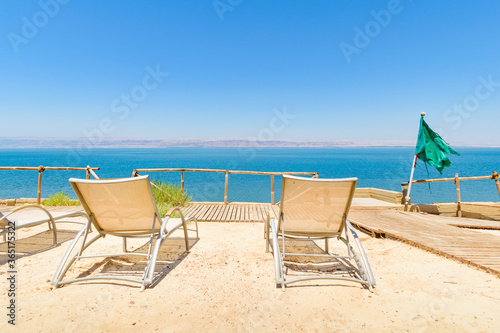 Rear view of two lounge chairs or tanning beds set on a sand terrace in a beach resort, overlooking the Dead Sea and Israel territories near Madaba, Jordan, Middle East