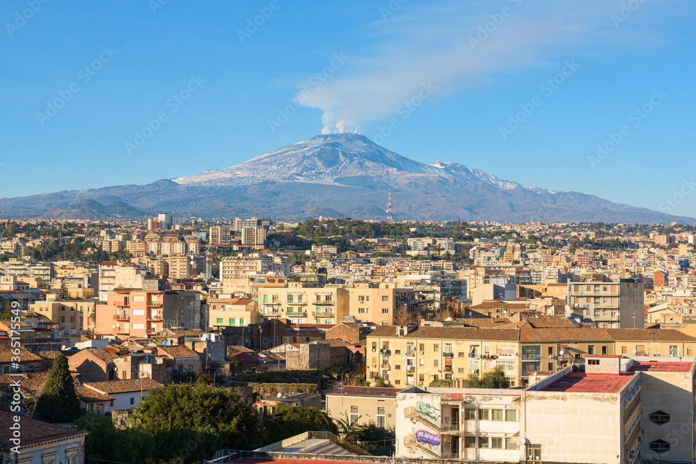Mount Etna volcano erupts over the skyline and rooftops of medieval city center of Catania, Sicily, Italy