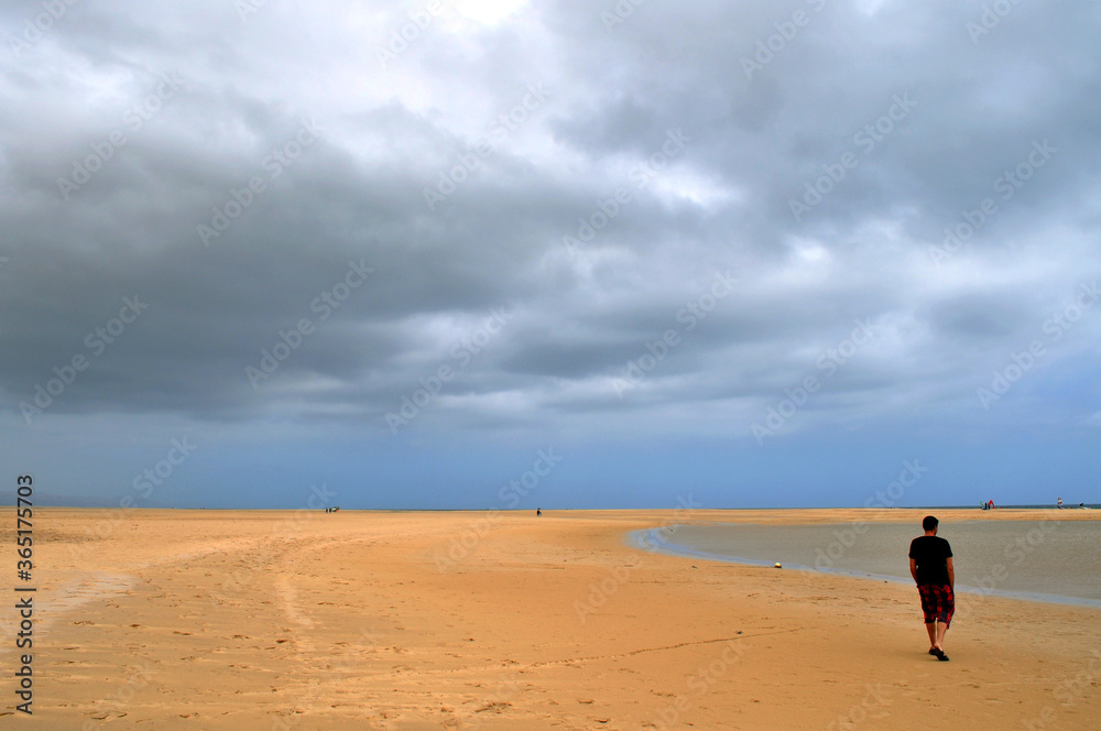 a man walks on a beautiful lonely beach with dark clouds in the sky, Sotavento, Fuerteventua, Canari Islands, Spain a man walks on a beautiful lonely beach with dark clouds in the sky, Sotavento, Fuerteventua, Canari Islands, Spain